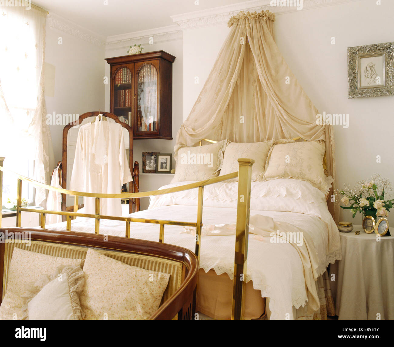 Coronet crème avec rideaux voile au-dessus de lit en laiton avec coussins crème et blanc duvet dans la chambre blanche Banque D'Images