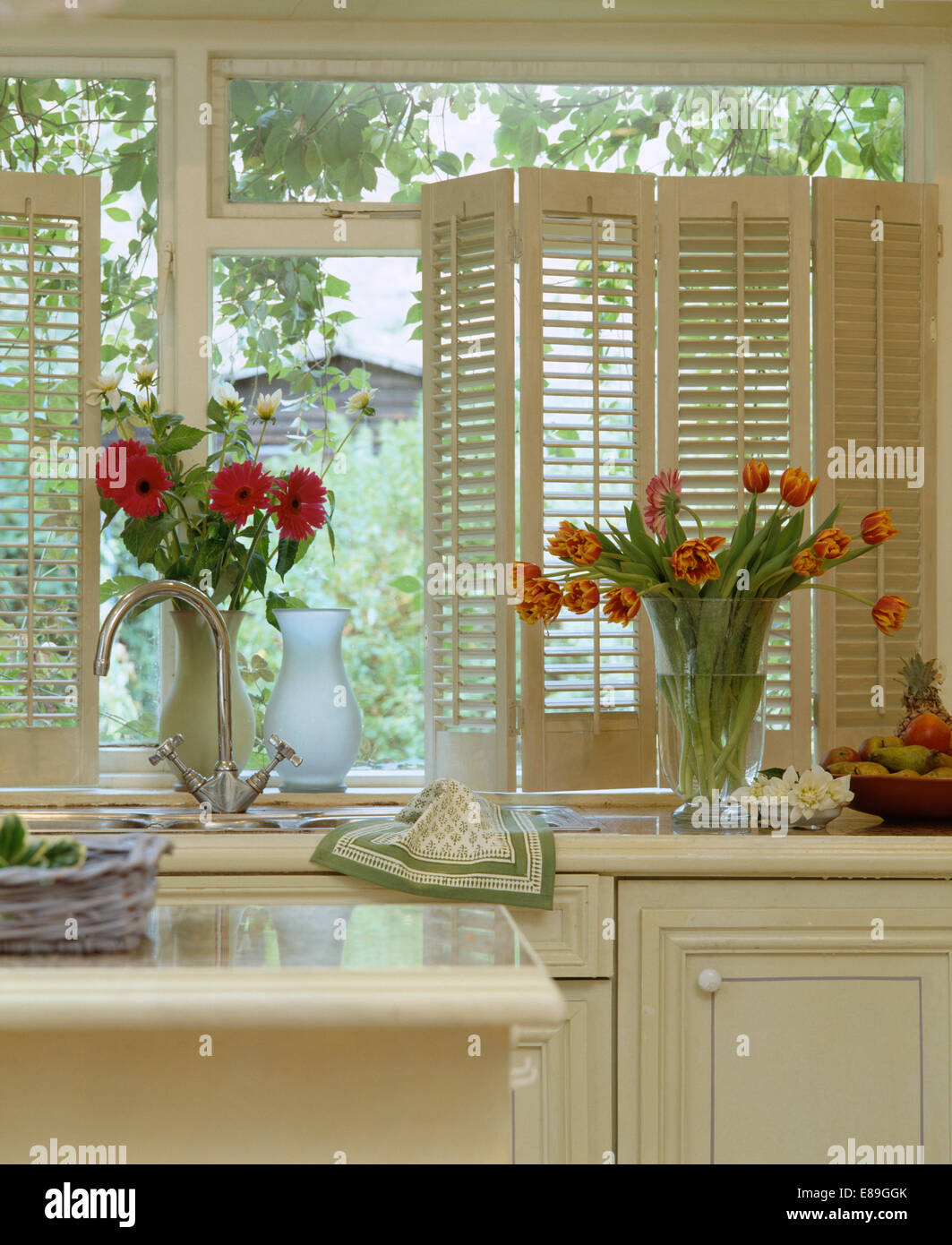 Gerberas rouges et orange striped tulips in vases de verre sur le rebord de la cuisine avec des obturateurs de plantation à la crème Banque D'Images