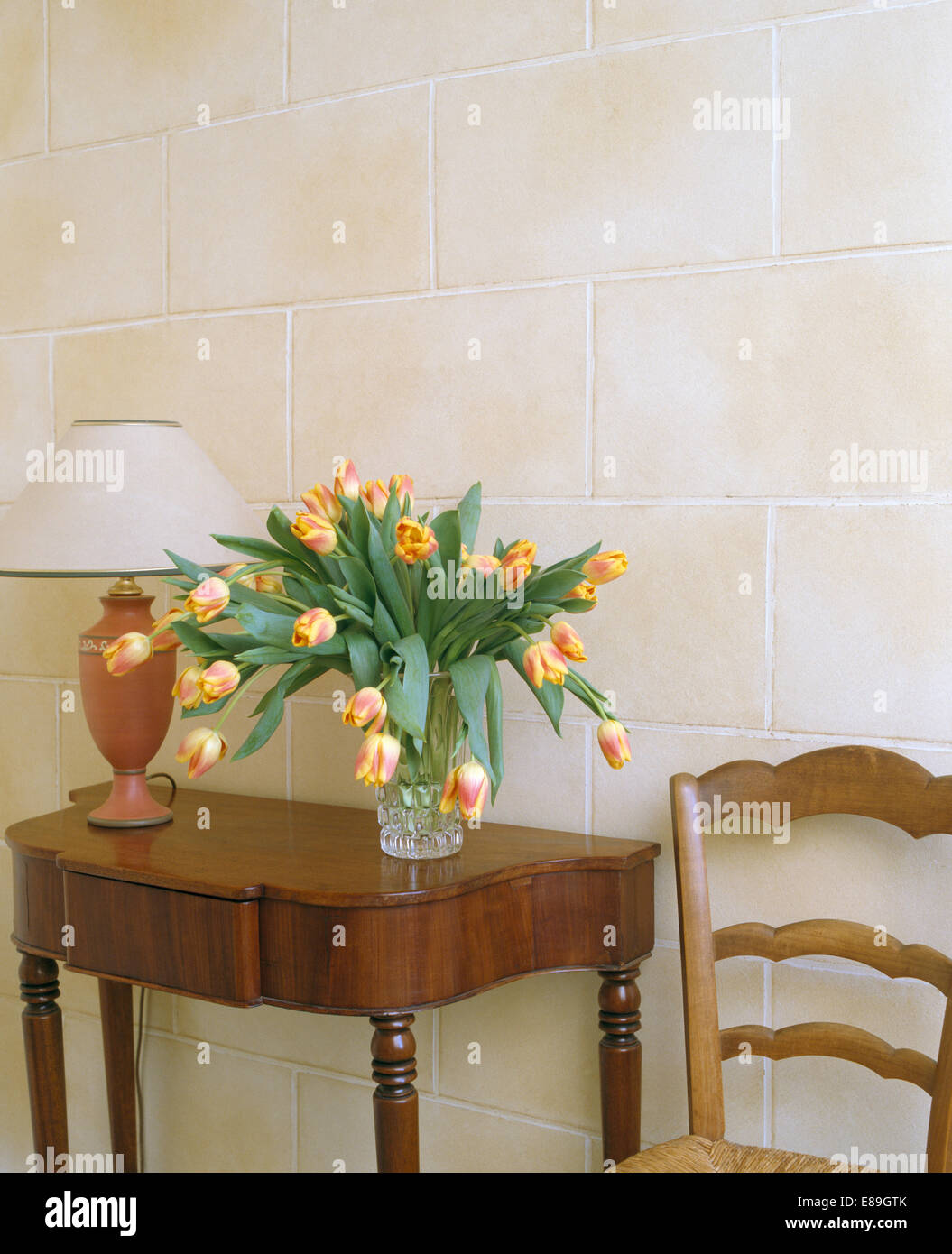 Close-up de vase de tulipes orange à côté de lampe sur console en acajou table en face du mur carrelé en travertin Banque D'Images