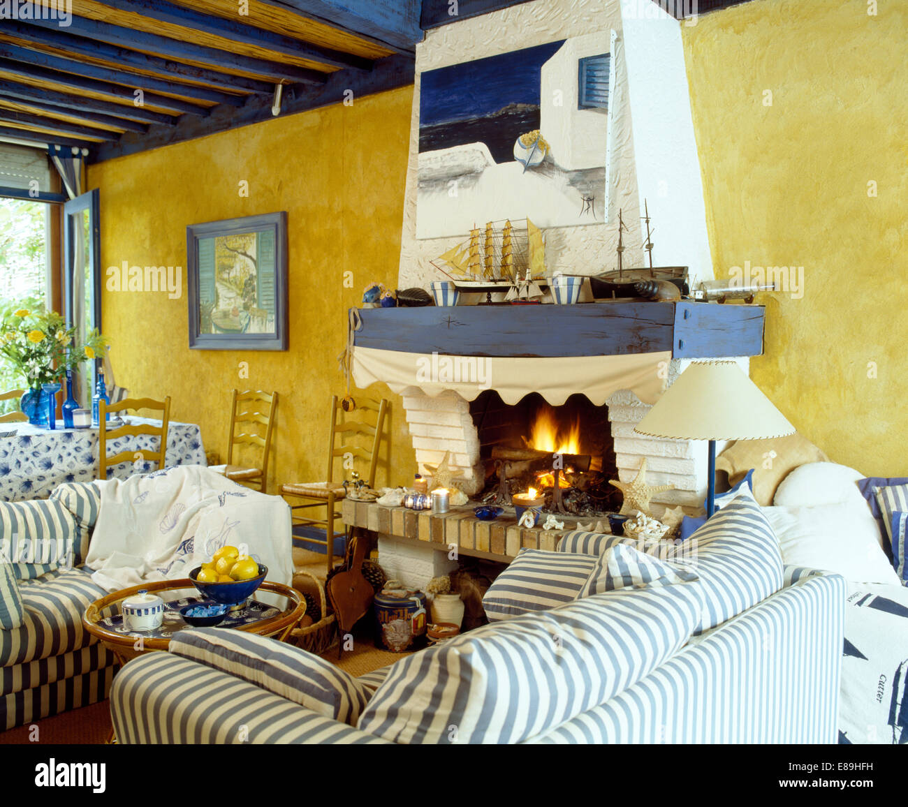 Canapés rayés bleus sur chaque côté de bleu et blanc peint en jaune cheminée salon du littoral Français Banque D'Images