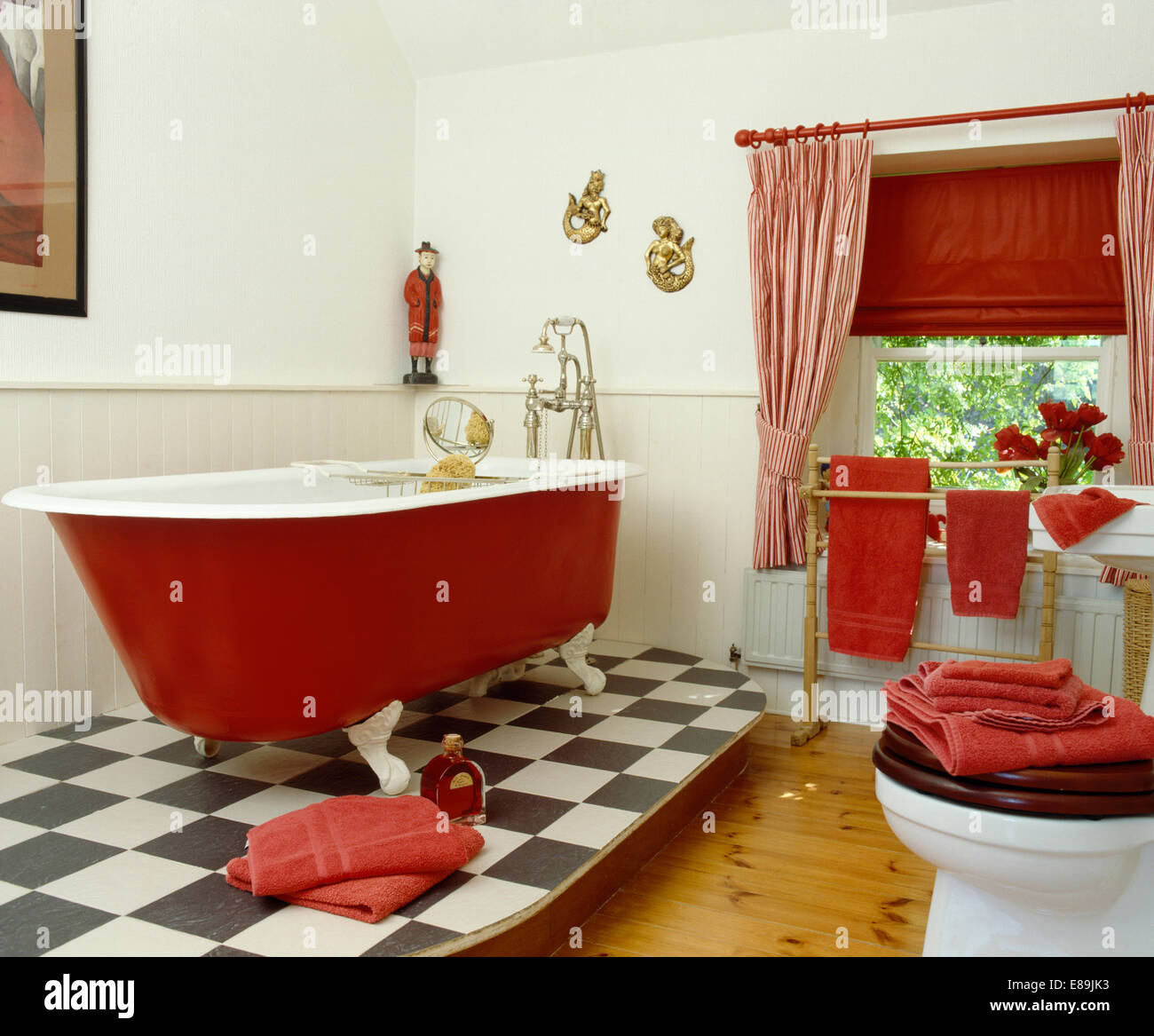 Couvercle cylindrique rouge noir +baignoire sur vinyle blanc marbre dans la salle de bains avec des rideaux à rayures rouge et aveugle sur la fenêtre Banque D'Images