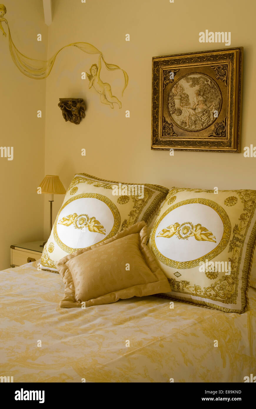 Chérubin peint et doré orné image encadrée au-dessus de lit avec coussins crème à motifs Banque D'Images