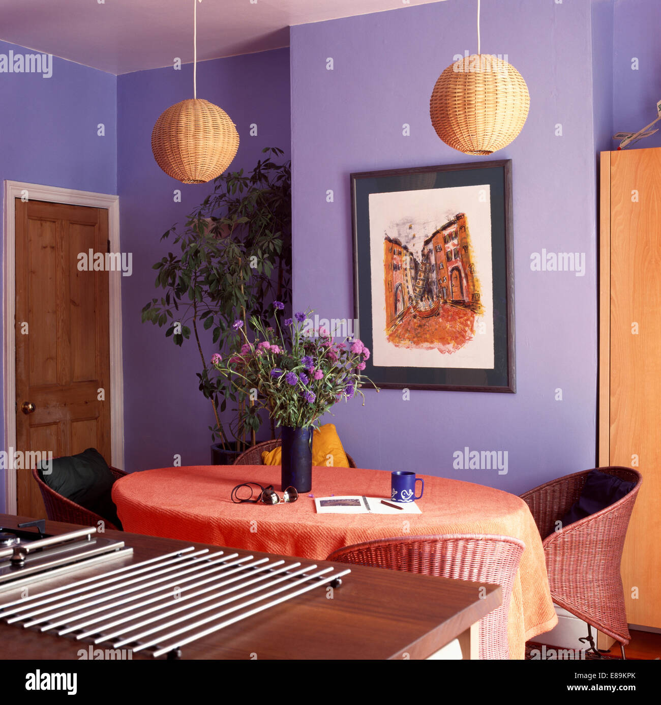 Nuances d'osier sur les lumières au-dessus de table avec tissu en lin orange mauve dans la salle à manger avec pot d'acier-tapis sur bahut Banque D'Images