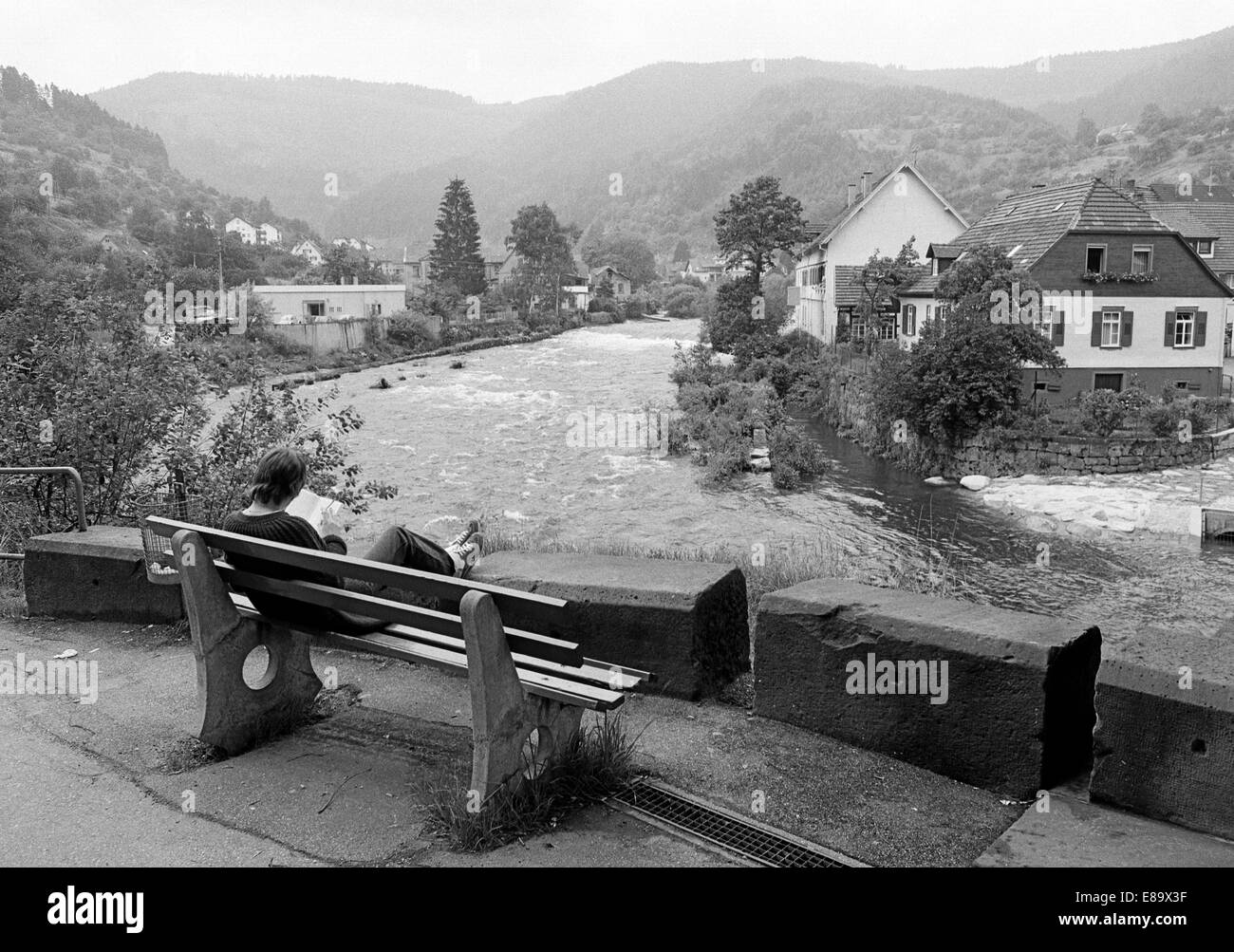 Achtziger Jahre, junge Frau auf einer Bank liest ein Buch, dahinter die Flusslandschaft der Murg und eine Mittelgebirgslandschaft, Forbach (Baden), Aucun Banque D'Images