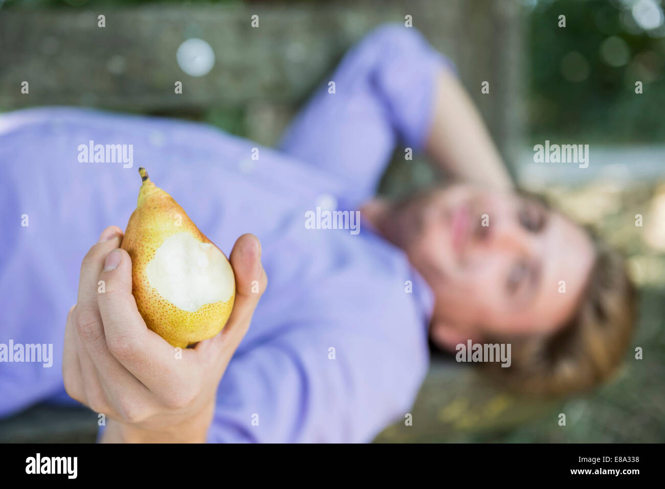 Mid adult man allongé sur le banc et poire alimentation Banque D'Images