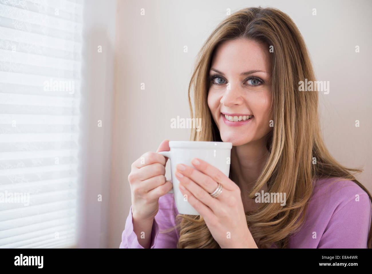 Smiling mature woman holding cup à la fenêtre Banque D'Images