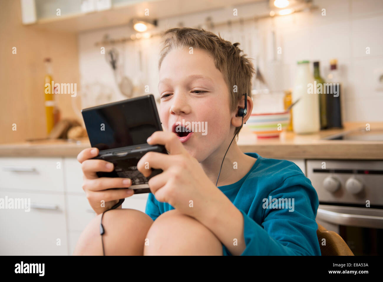 Boy playing video game in kitchen Banque D'Images Boy playing video game in kitchen Banque D'Images