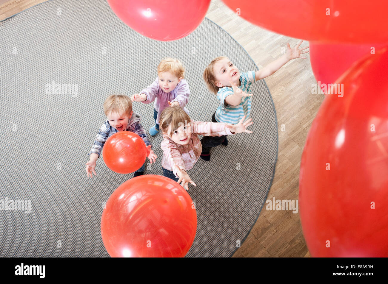 Quatre enfants qui jouent avec des ballons rouges en maternelle, elevated view Banque D'Images