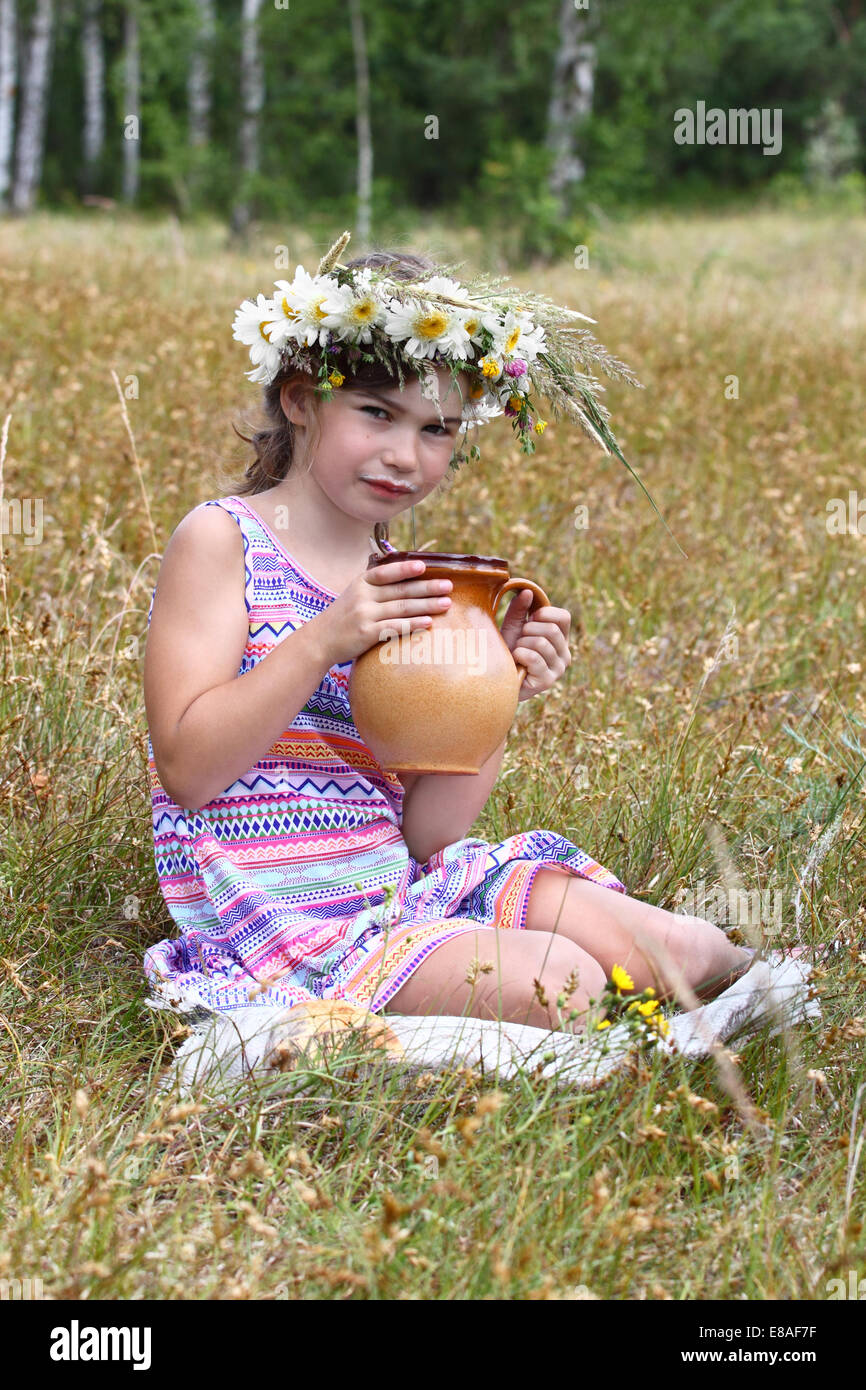 Petite fille assise sur l'herbe avec verseuse en mains. Ses lèvres des traînées dans le lait Banque D'Images