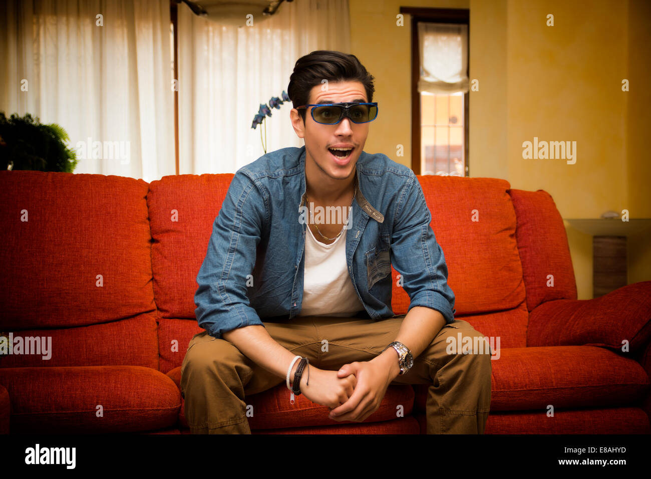 Jeune homme portant des lunettes 3D réagissant de surprise et d'excitation  comme il est assis sur un canapé à la maison à regarder un programme de  télévision Photo Stock - Alamy