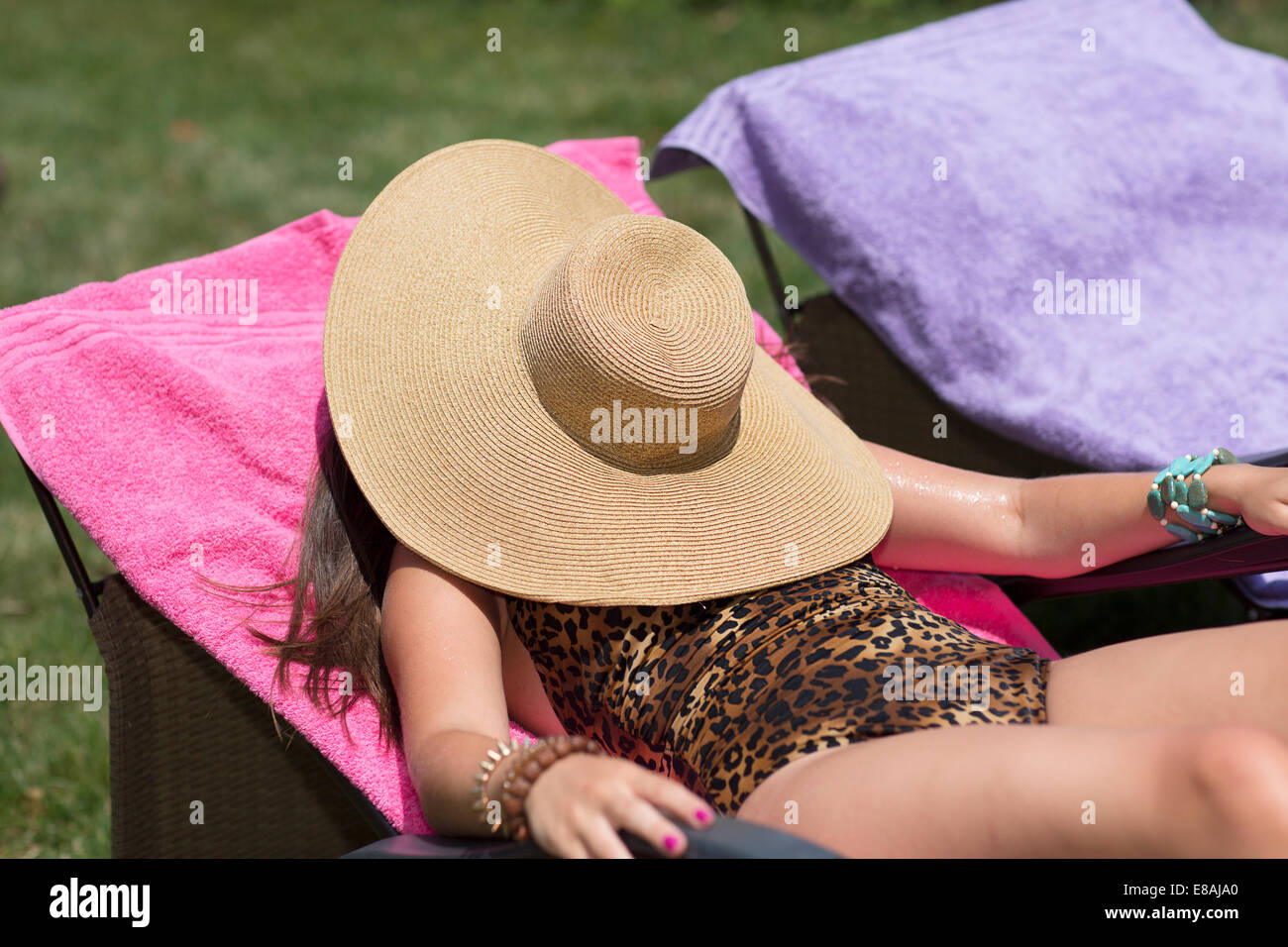 Jeune femme se cachant sous chapeau contre le soleil sur une chaise longue dans le jardin Banque D'Images