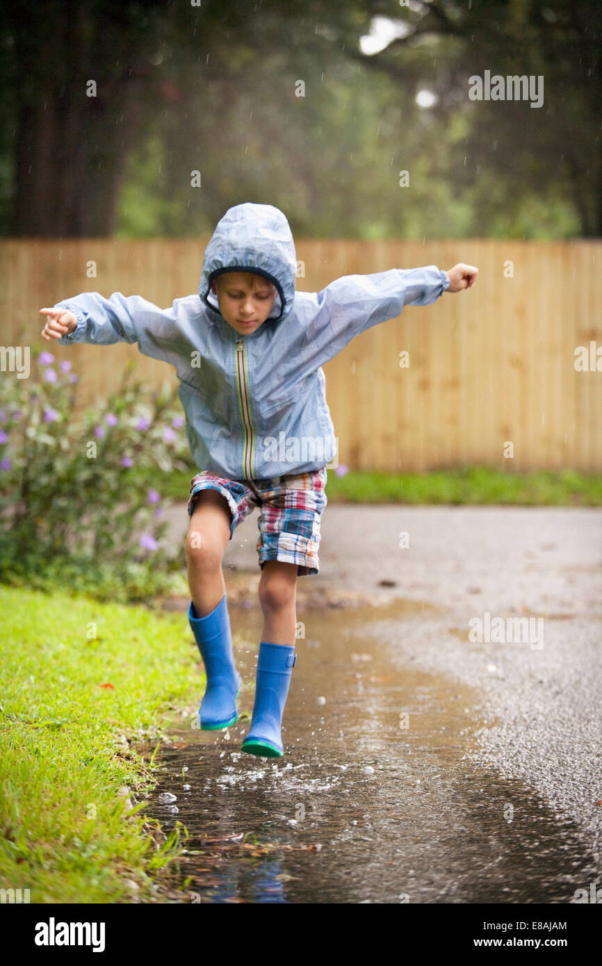 En bottes de caoutchouc garçon sautant dans la pluie flaque Banque D'Images