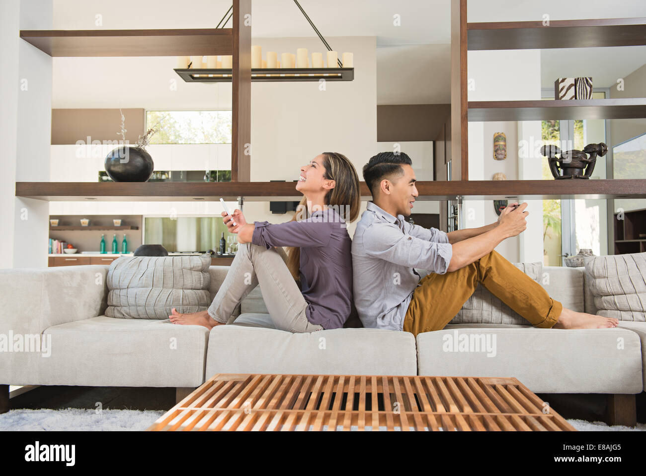 Couple assis dos à dos jouer aux jeux sur smartphones sur salon canapé Banque D'Images