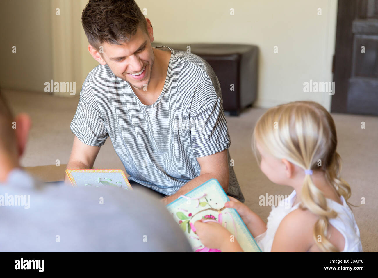 Homme couple et sa fille l'enfilage des livres d'images dans la salle de séjour Banque D'Images