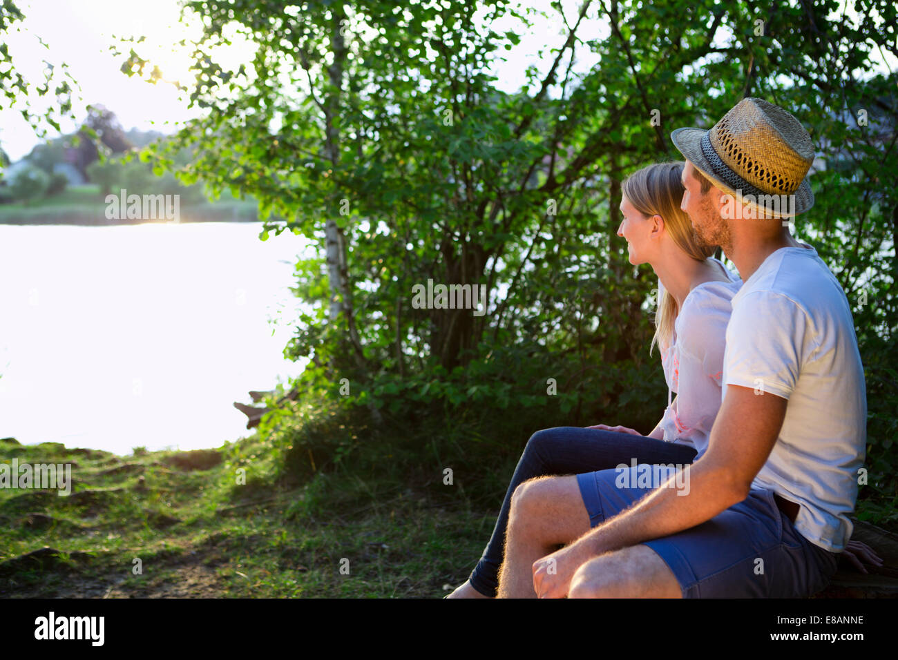 Young couple sitting by lake regardant le coucher du soleil Banque D'Images