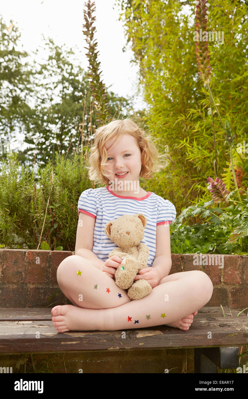 Portrait de fille sur le siège de jardin avec l'ours en peluche et les étoiles autocollants sur les jambes Banque D'Images