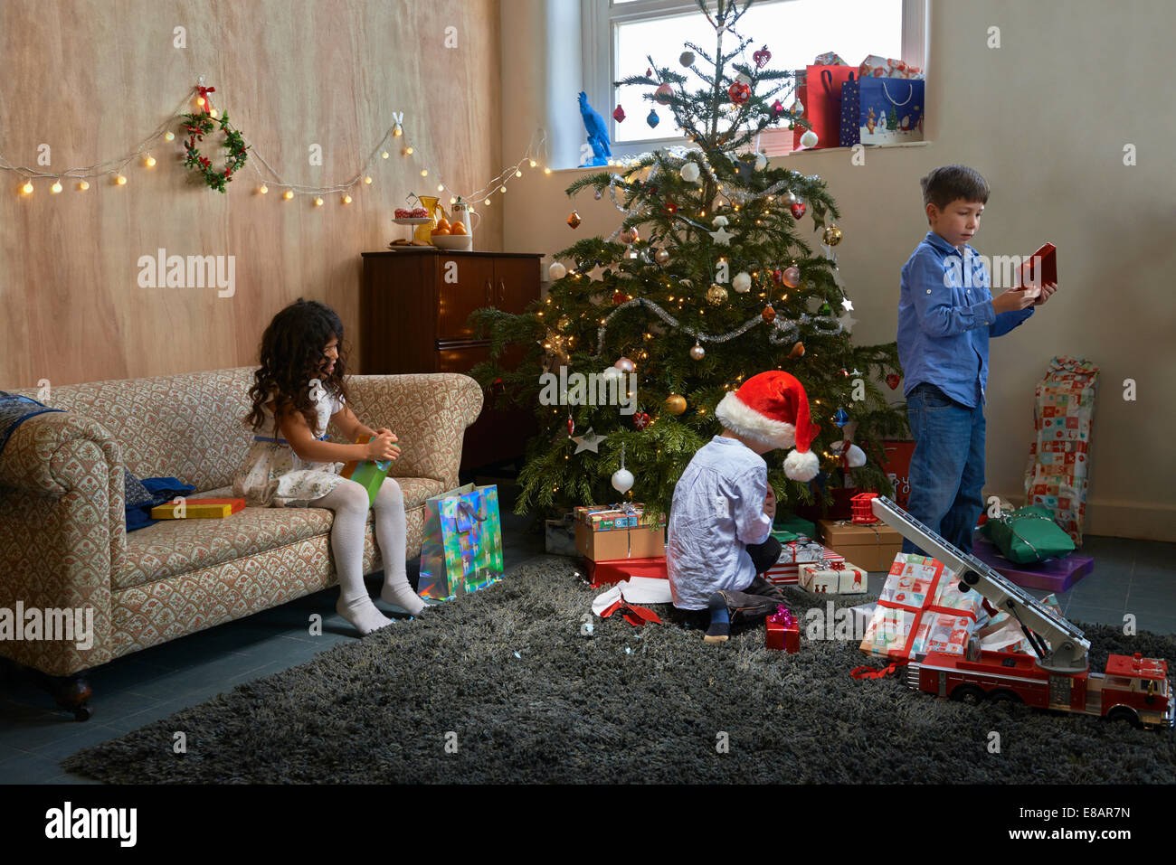 Fille et deux frères d'ouvrir les cadeaux de Noël dans la salle de séjour Banque D'Images