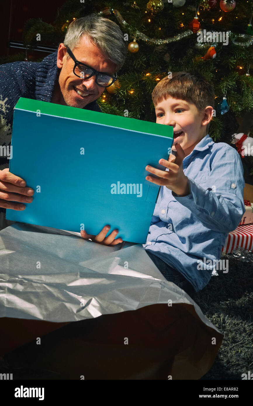 Père sur l'ouverture du plancher salon des cadeaux de Noël avec fils Banque D'Images