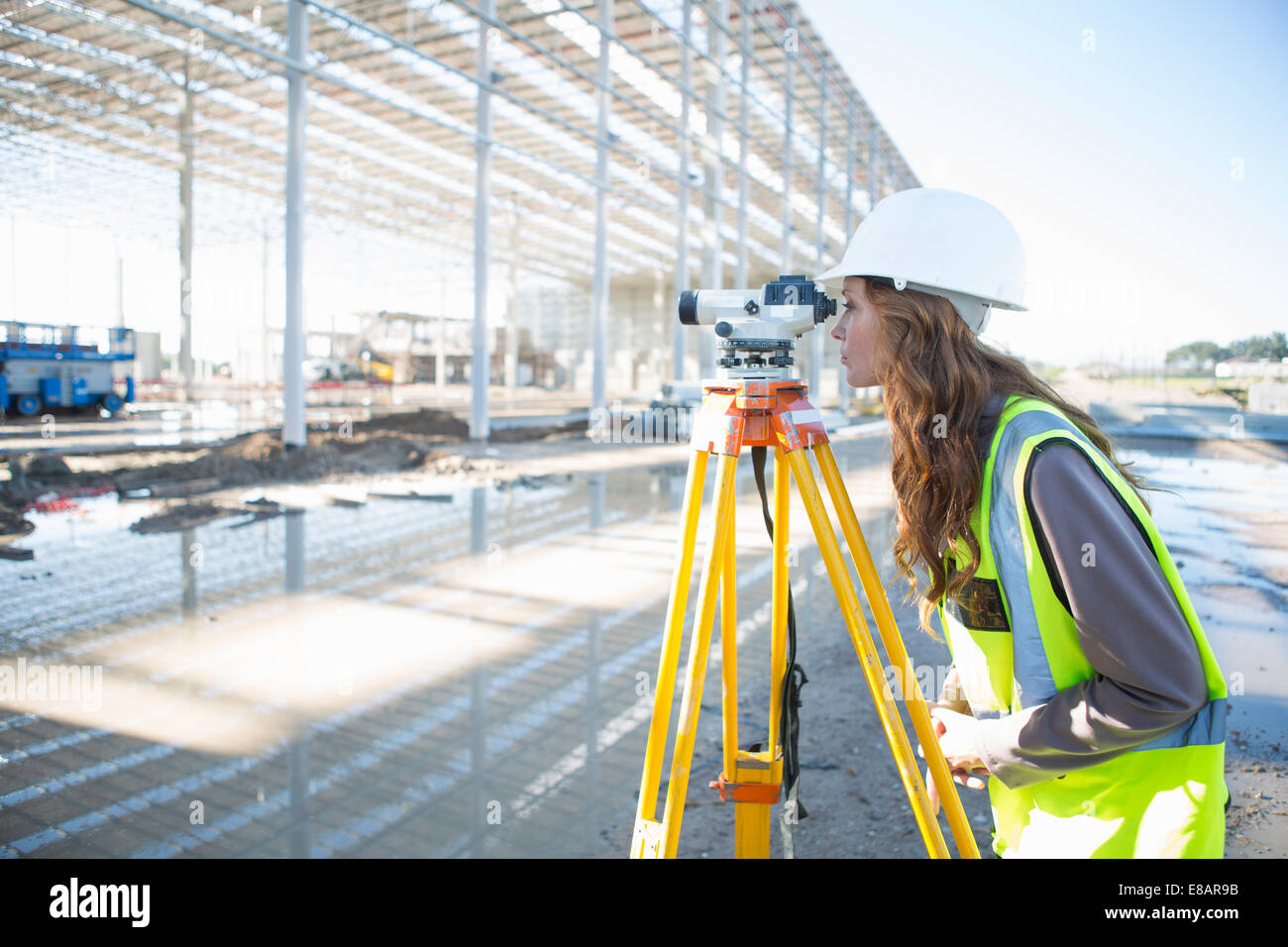 Surveyor se pencher en avant pour regarder à travers le niveau construction site Banque D'Images