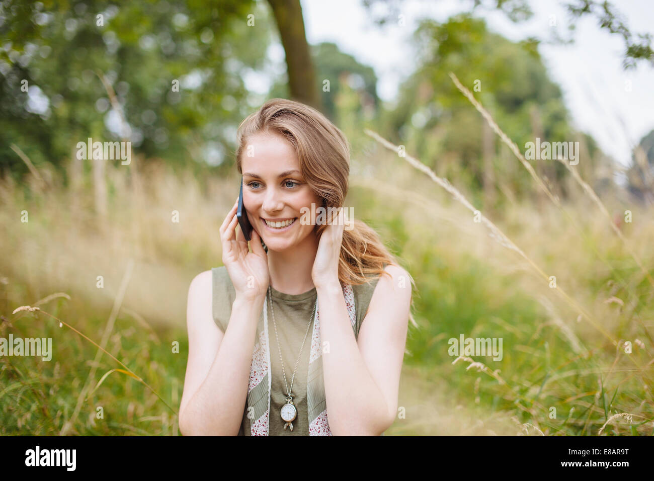 Young woman chatting on smartphone in field Banque D'Images