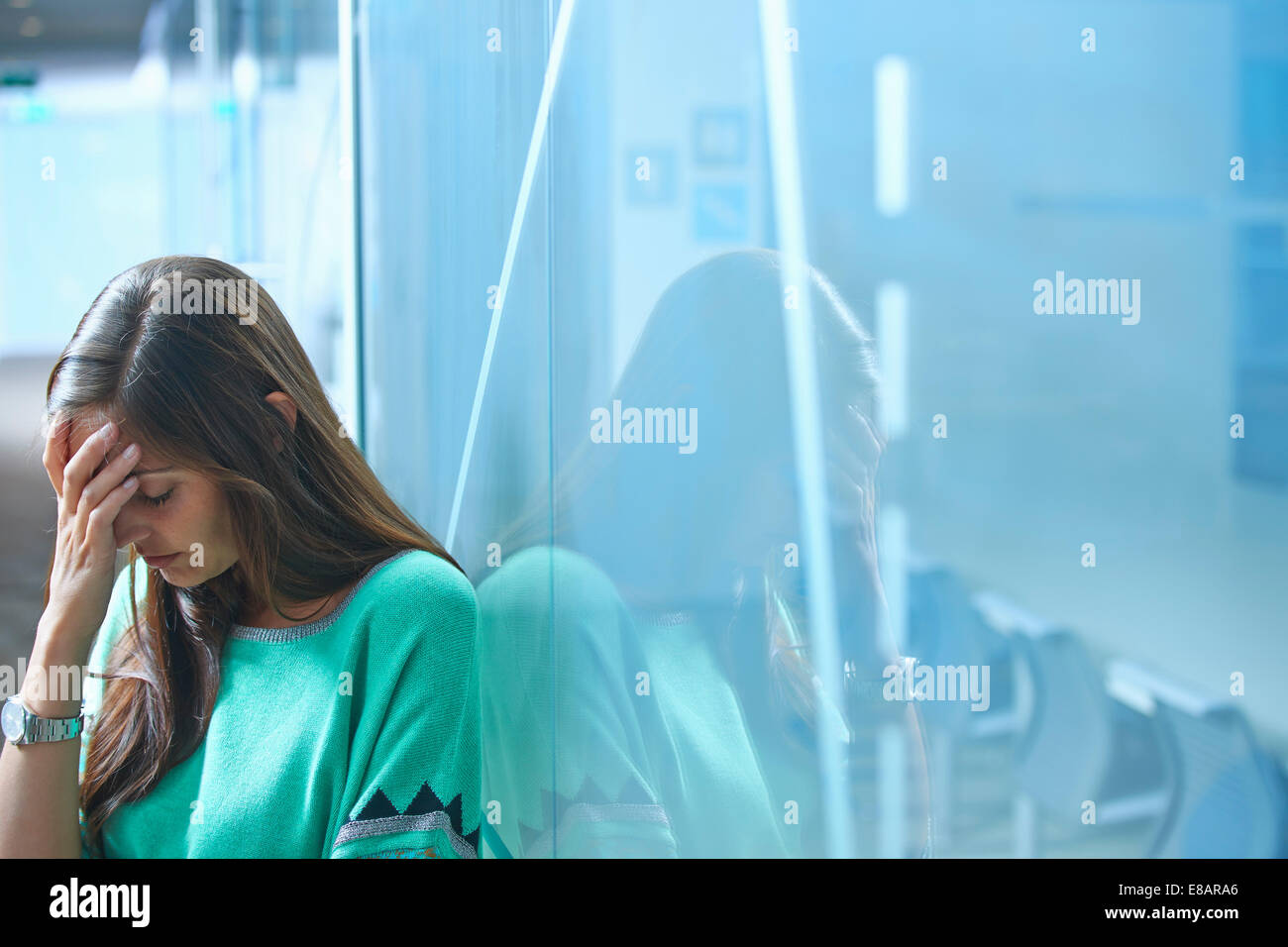 Mid adult businesswoman leaning against glass wall in office with hand on face Banque D'Images