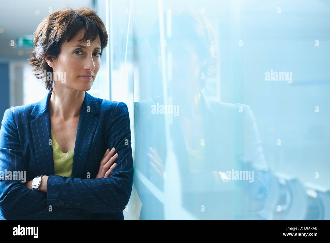 Portrait of mature businesswoman leaning against glass wall with arms crossed Banque D'Images