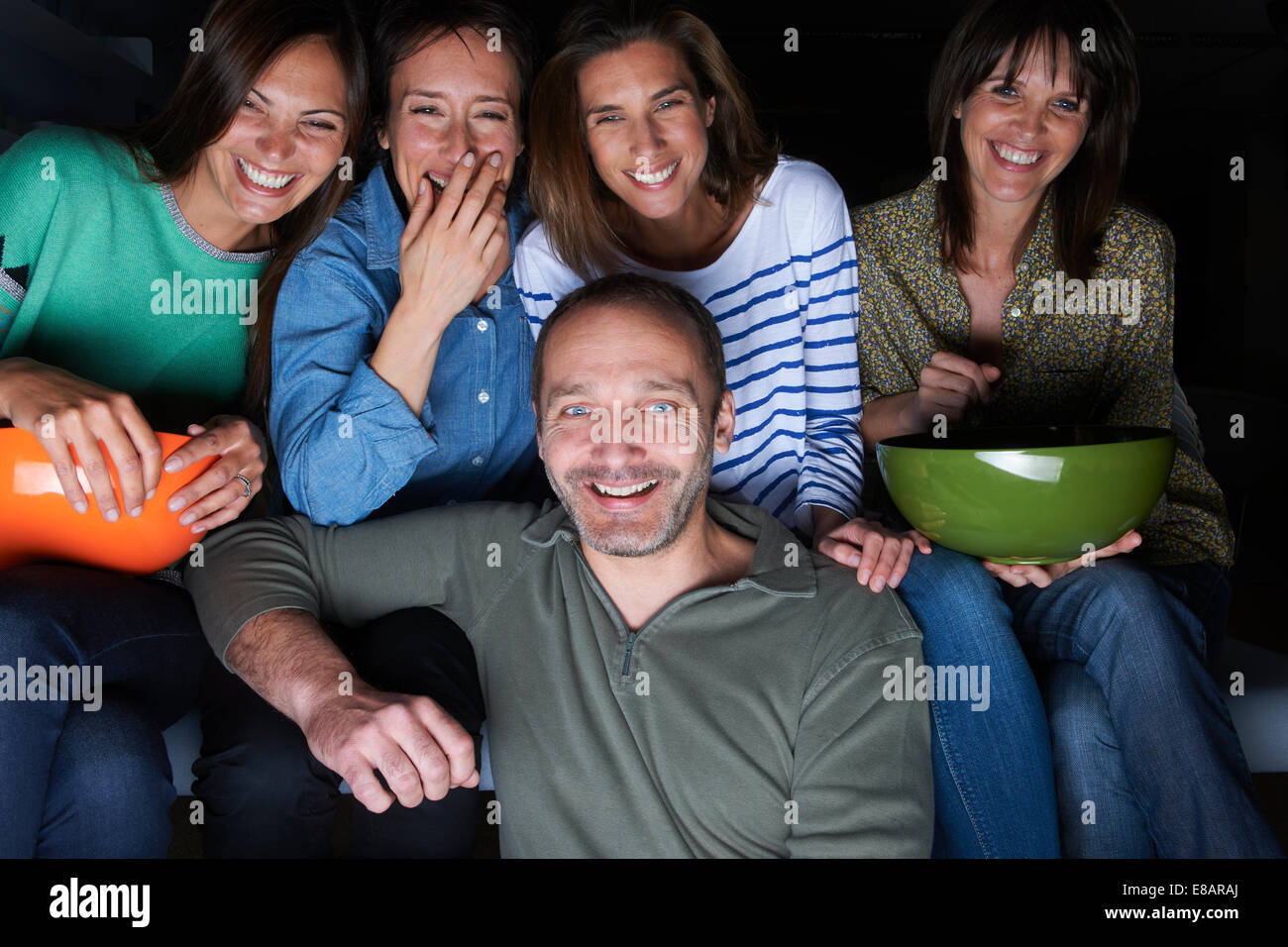 Cinq amis adultes rire et regarder la TV avec snack-bowls Banque D'Images