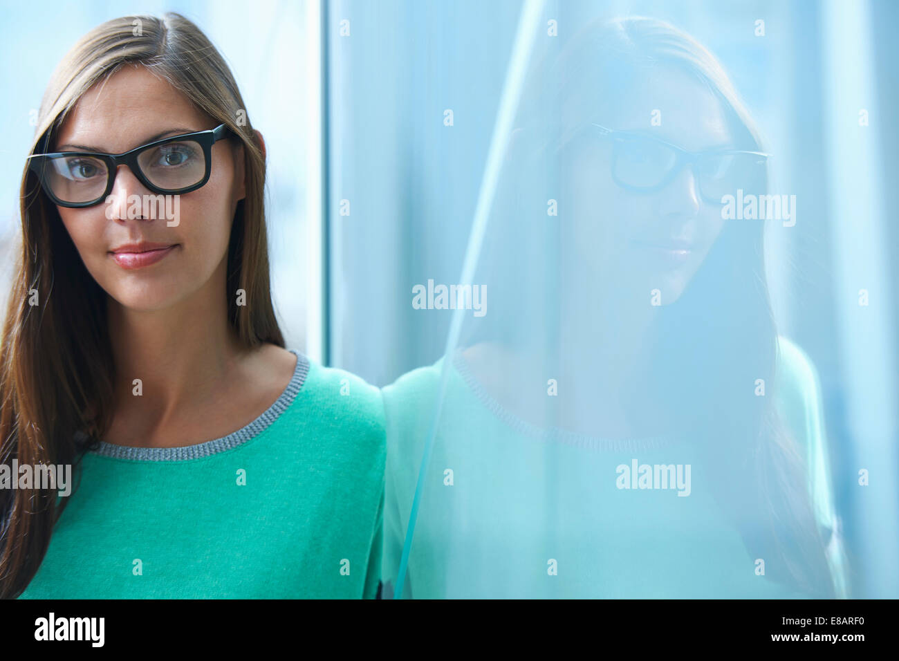 Portrait of mid adult businesswoman leaning against glass wall in office Banque D'Images