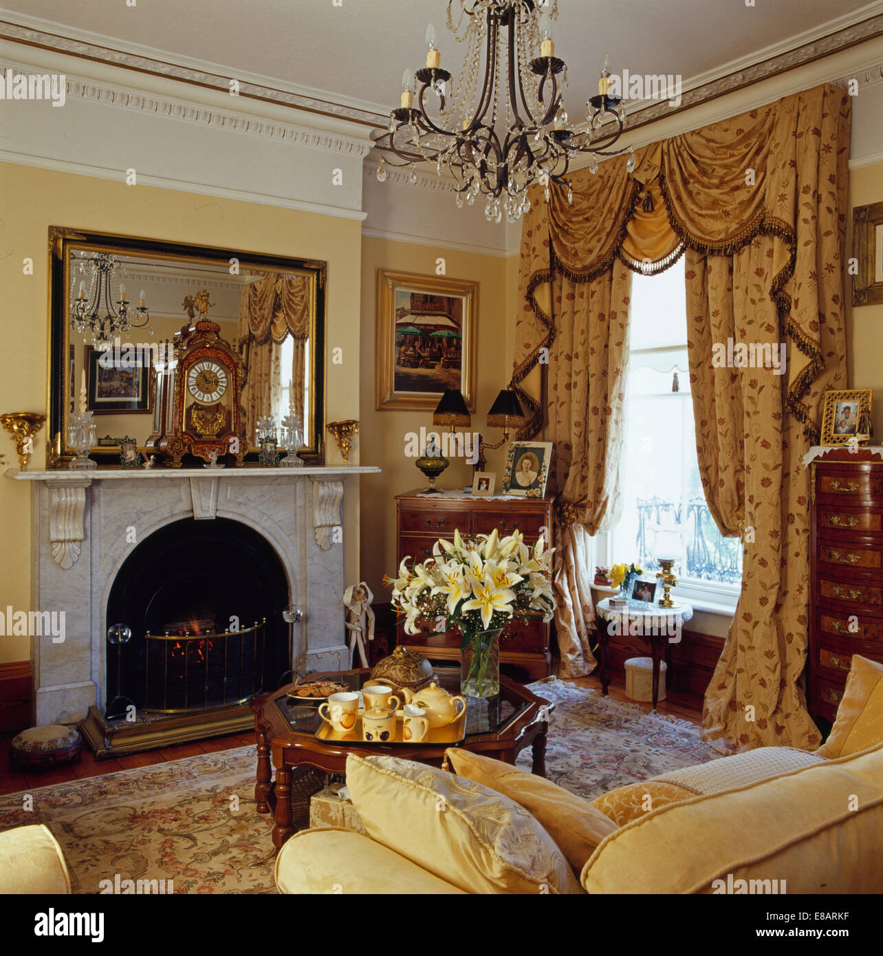 Grand miroir au-dessus de la cheminée de marbre en jaune salon avec rideaux opulents swagged +queue sur la fenêtre Banque D'Images