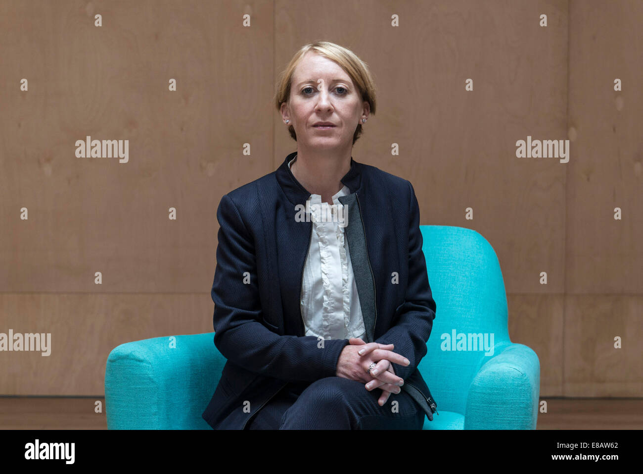 Une entreprise aux cheveux courts femme assise dans un fauteuil bleu couleur funky avec les jambes pliées dans un costume d'affaires dans une salle de réunion Banque D'Images