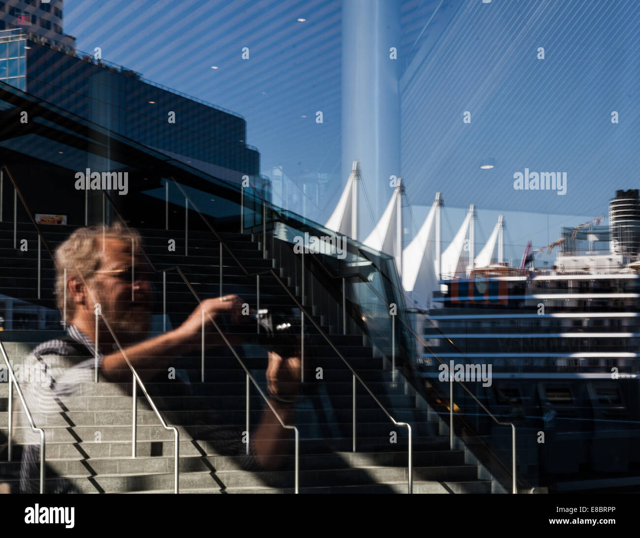 Un touriste mâle avec un appareil photo prenant une photo; le reflet de BC place, les voiles du bâtiment, et un bateau de croisière visible Banque D'Images