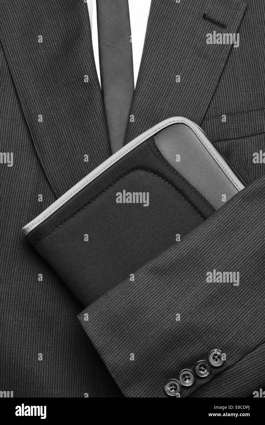 Close up of a man's costume avec chemise blanche et cravate et veste pliée sur le bras un petit ordinateur portable. Format vertical en noir et Banque D'Images