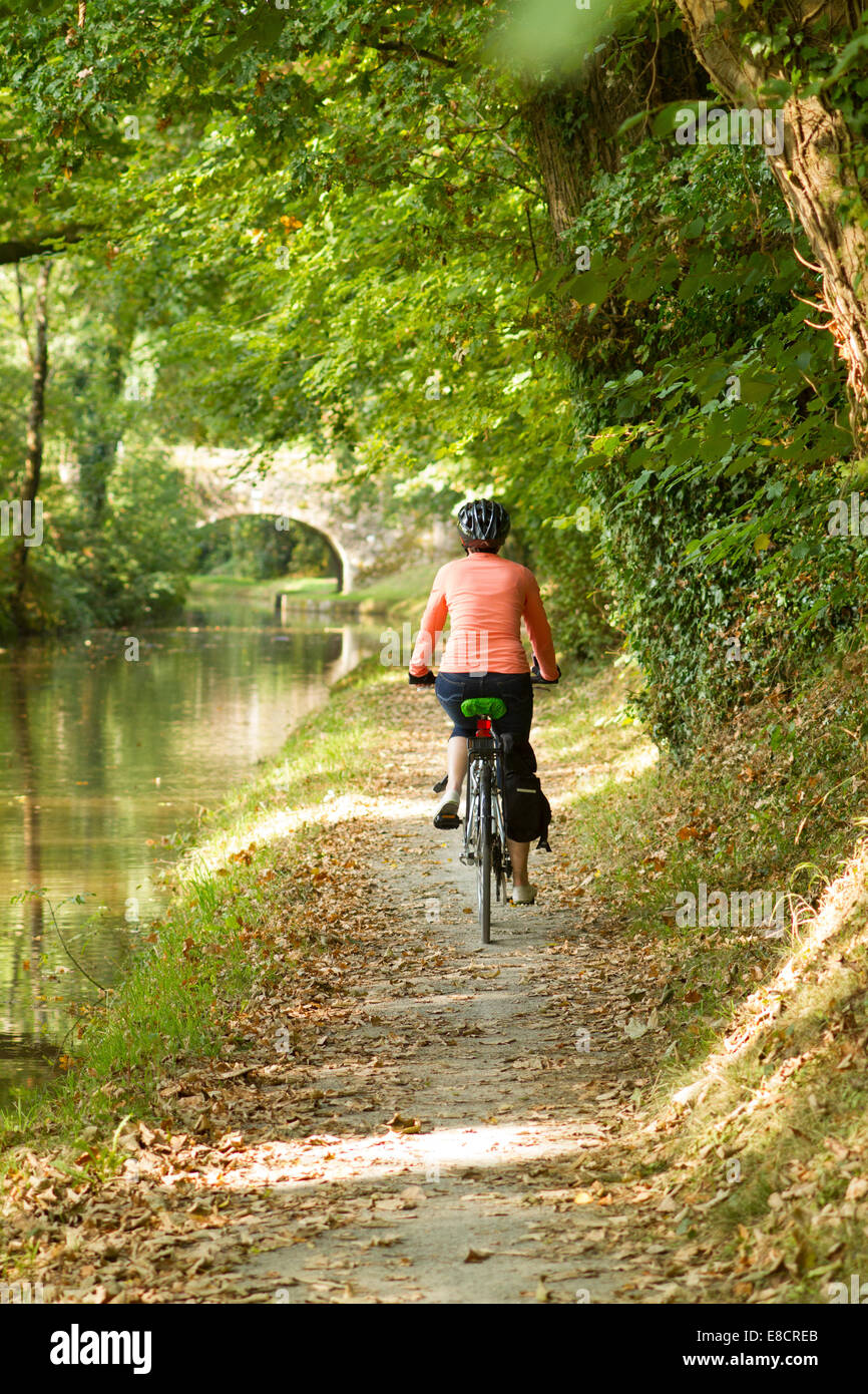 Jeune femme à vélo sur un chemin de halage du canal Banque D'Images