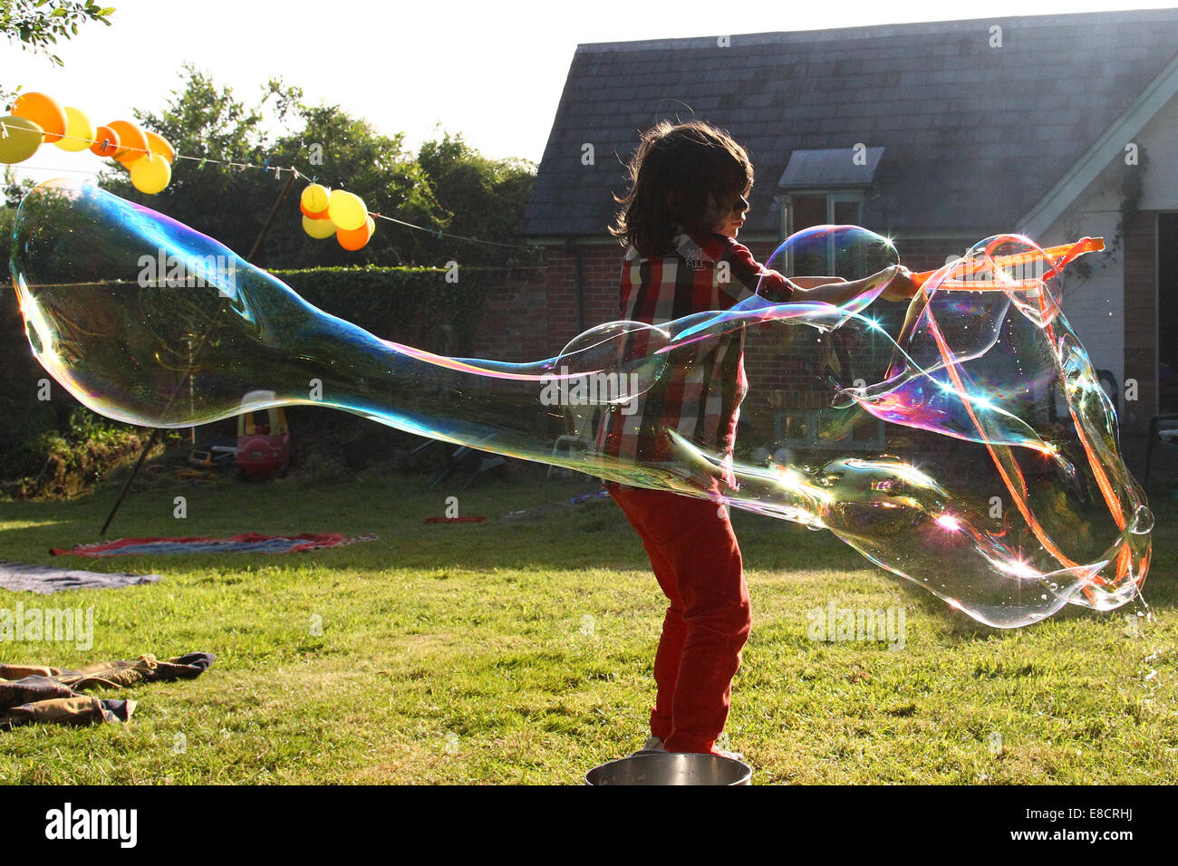 Un jeune enfant faire des bulles dans un jardin sur un jour d'été au cours d'une garden party. Banque D'Images
