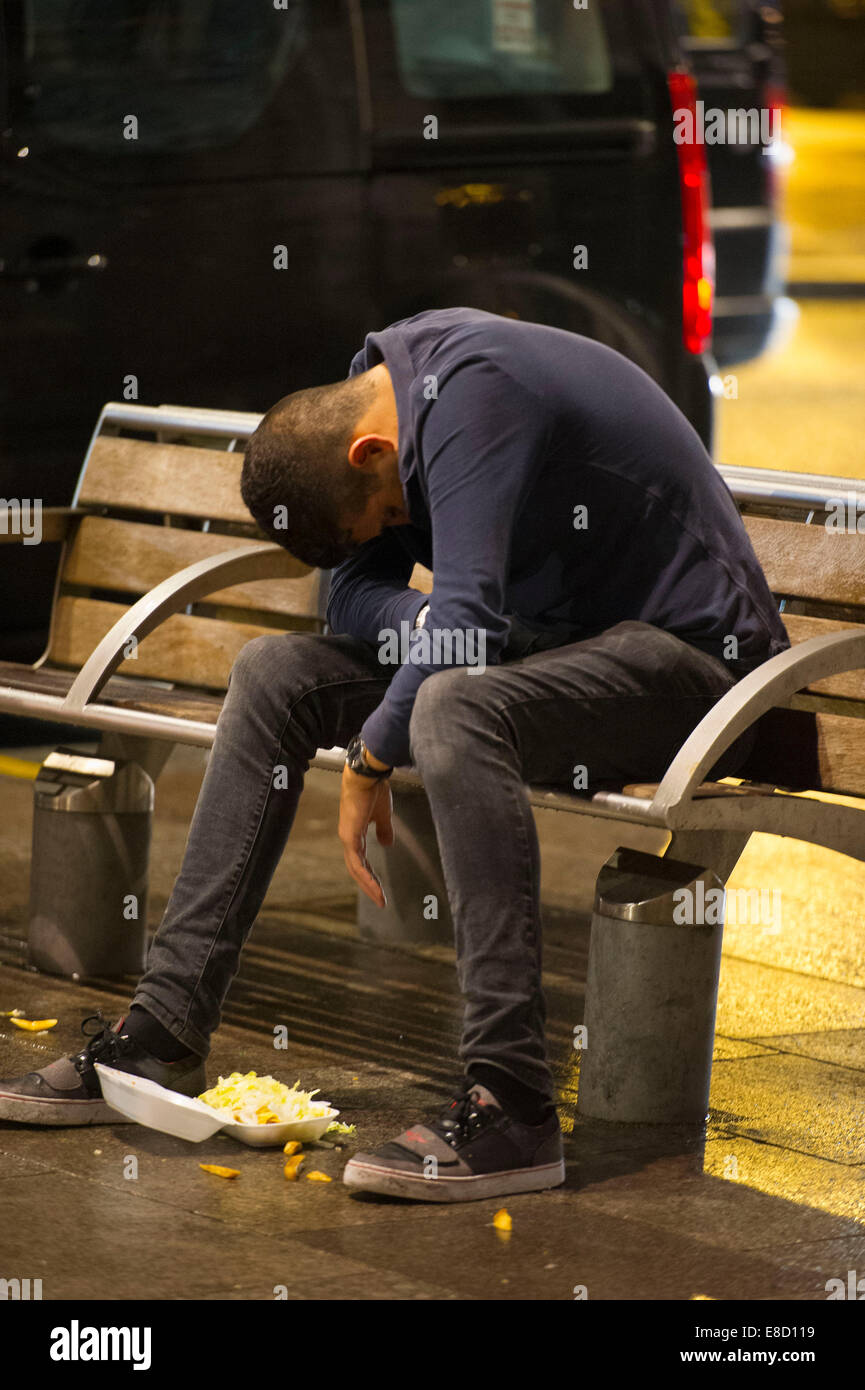 Un slouches jeunesse ivre sur un banc après une nuit de forte consommation excessive d'alcool. Banque D'Images