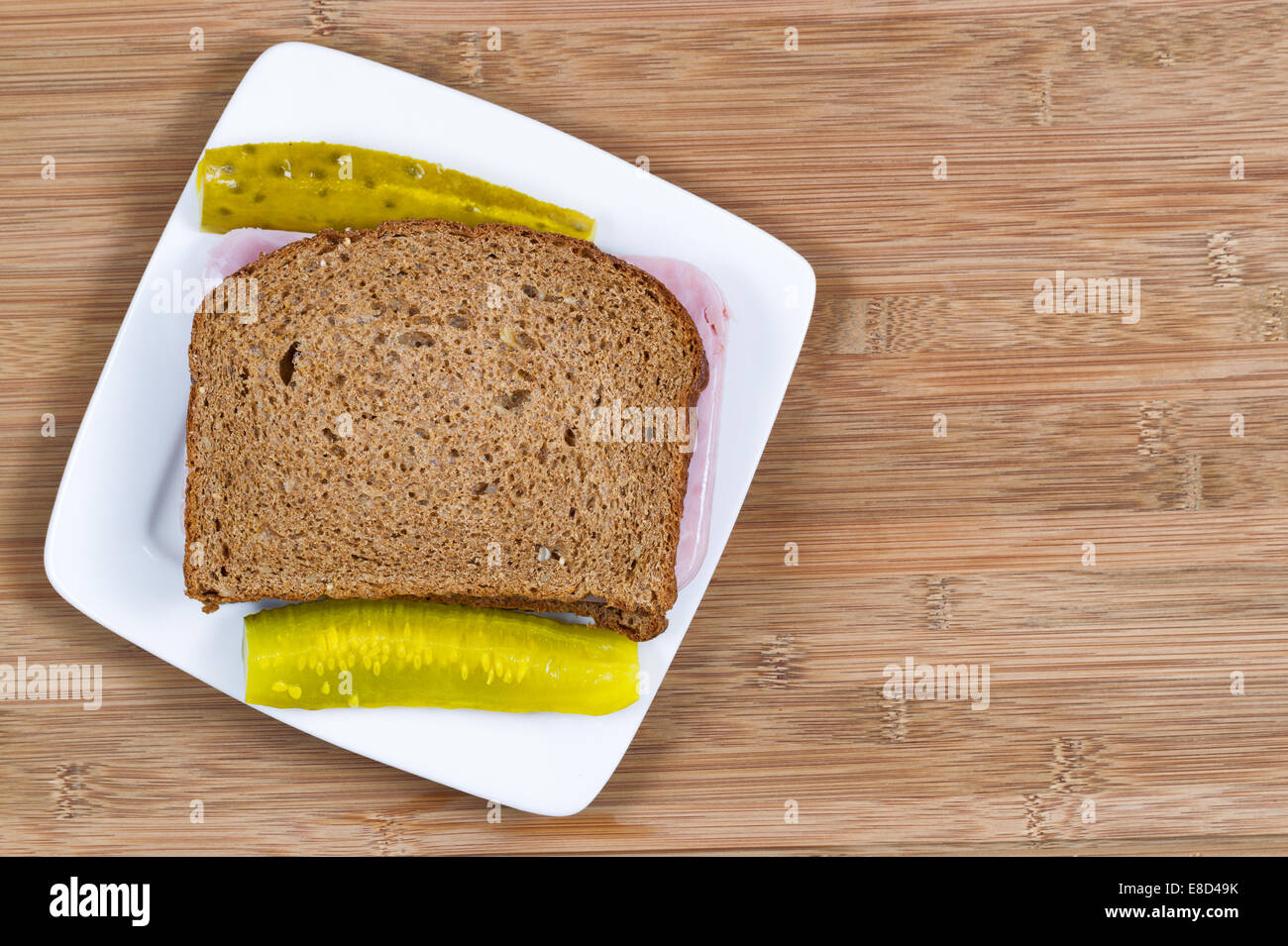 Vue du dessus de l'horizontale Gros plan Ham sandwich fait de pain de blé entier et des cornichons sur le côté avec plaque blanche et bois Banque D'Images