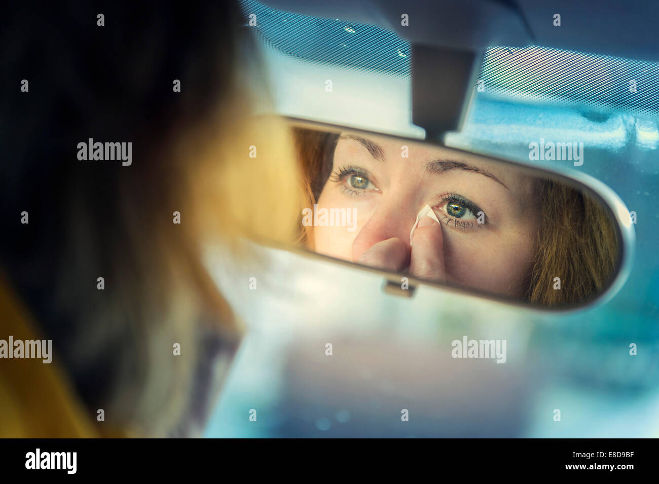 Jeune femme à la recherche d'elle-même dans un rétroviseur tout en tapotant ses larmes, Allemagne Banque D'Images