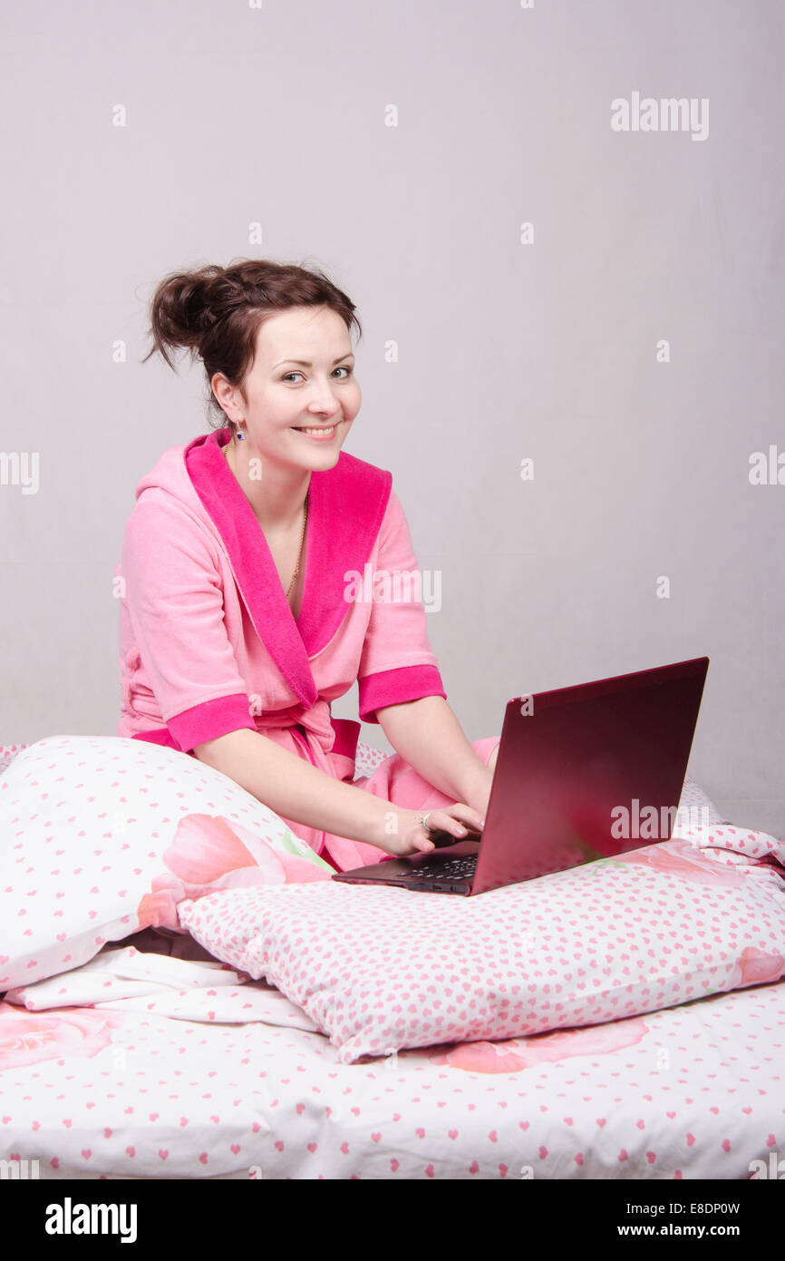La jeune fille s'assit dans le lit et travaille à l'ordinateur portable Banque D'Images