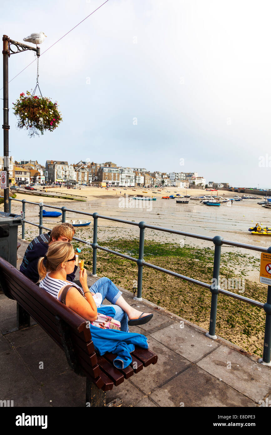 La consommation de crème glacée à la ville portuaire de St Ives, Cornwall UK couple assis sur le banc face à Harbour Banque D'Images