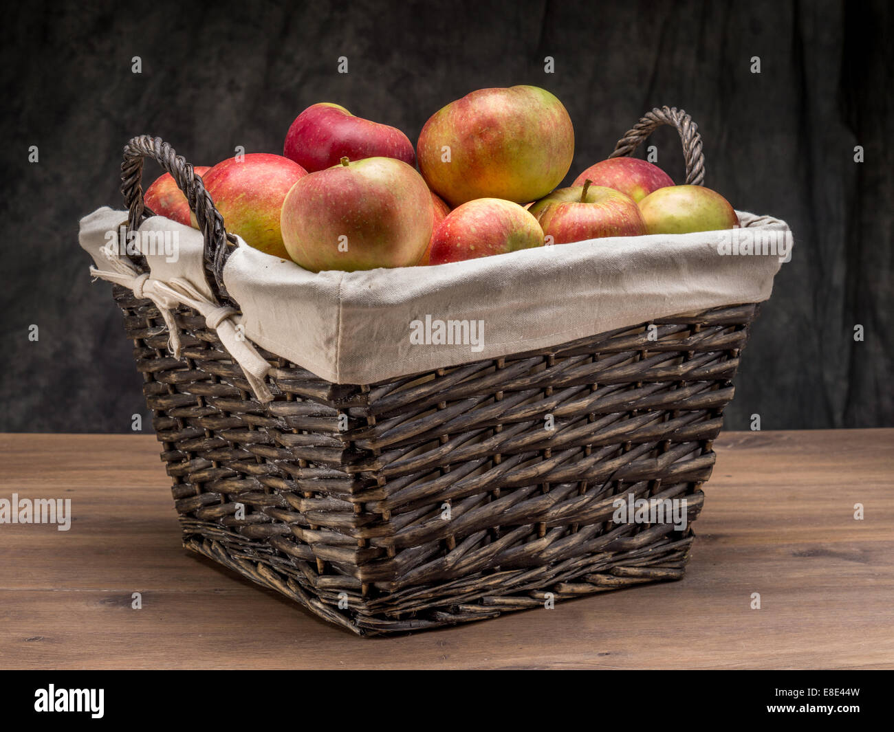 Panier en osier rempli de pommes delicious tourné sur fond gris foncé Banque D'Images