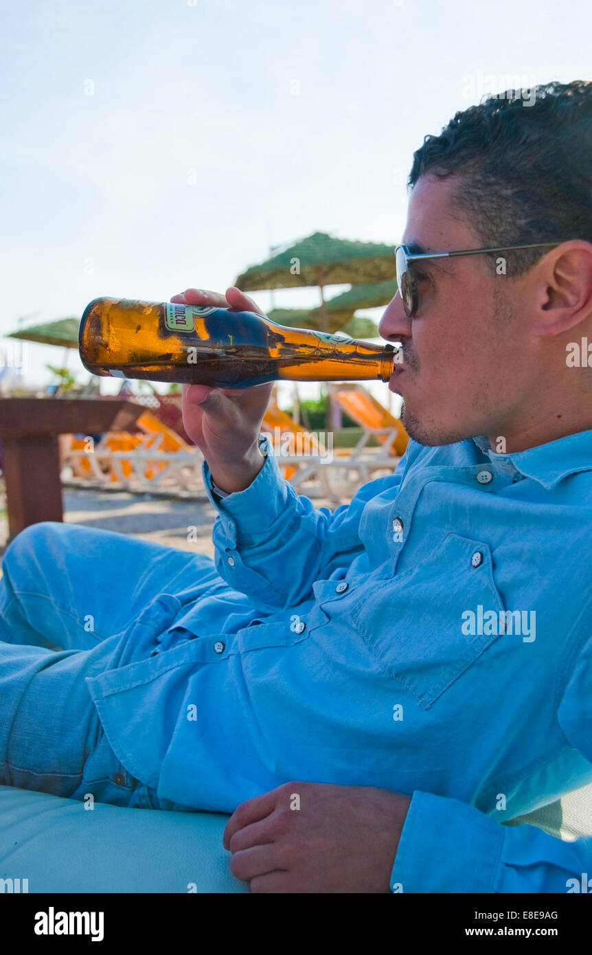 Portrait vertical d'un jeune homme marocain attrayant de boire une bière sur une plage. Banque D'Images