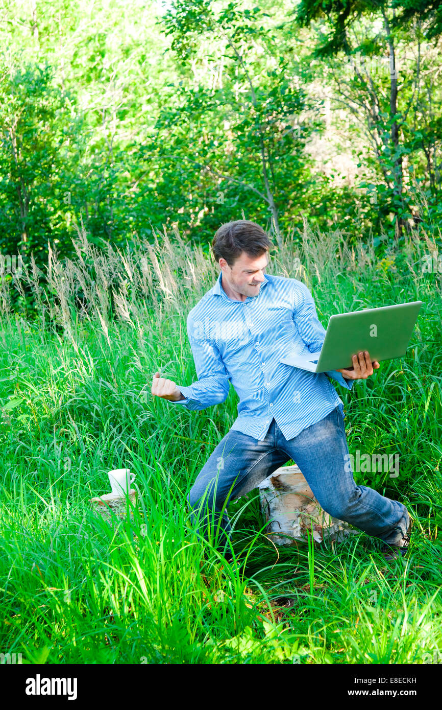 Super homme heureux dans la forêt avec un ordinateur portable... c'est un succès ! Banque D'Images