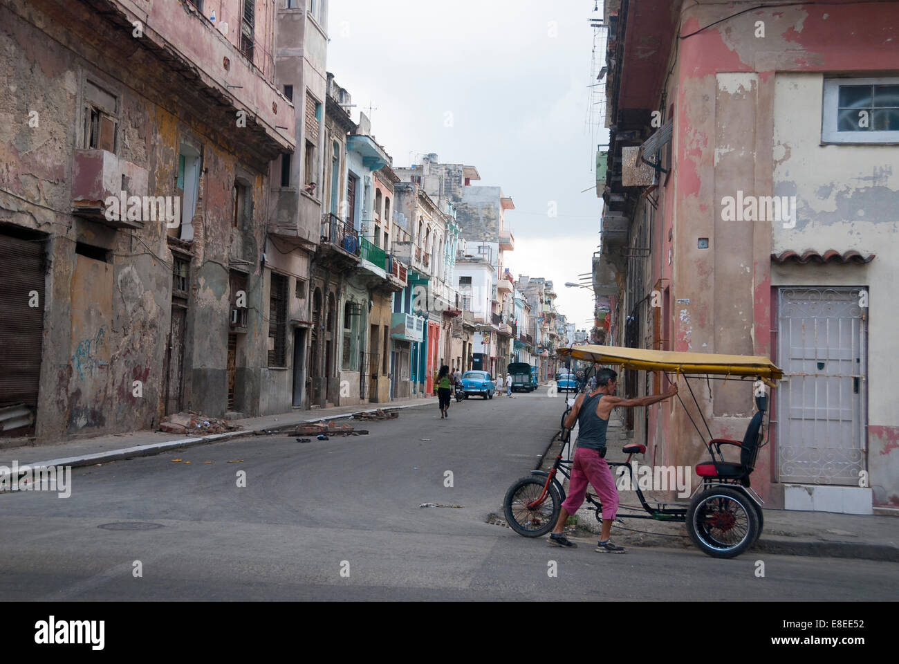 Un homme son parking vélo taxi entre les vieux bâtiments en ruine dans un quartier de La Havane Banque D'Images