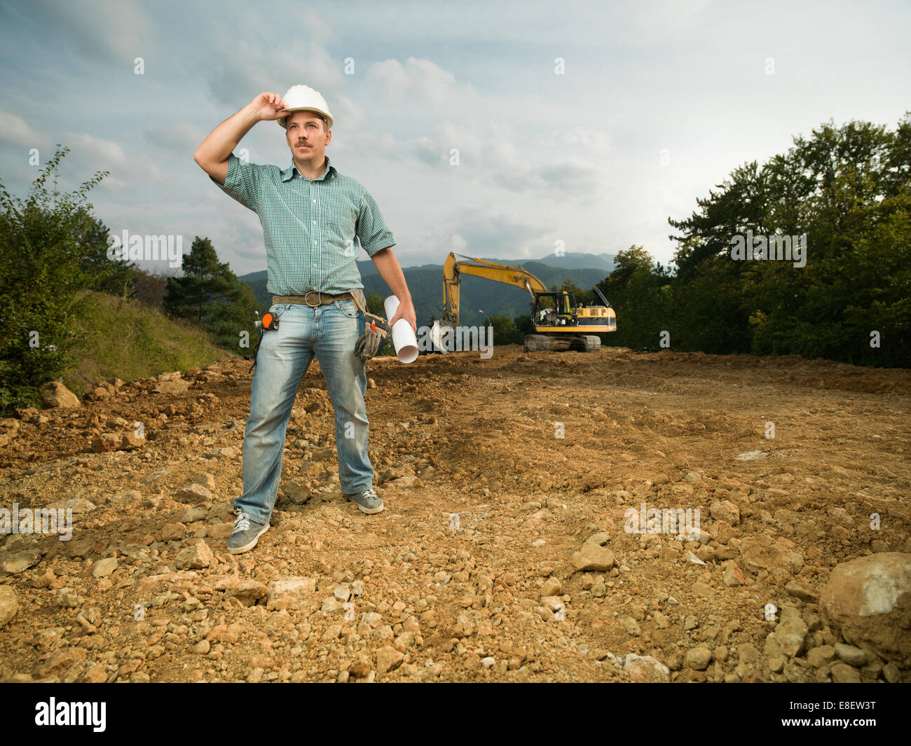 Vue avant de l'homme permanent ingénieur sur site de construction holding blueprint et casque Banque D'Images Vue avant de l'homme permanent ingénieur sur site de construction holding blueprint et casque Banque D'Images