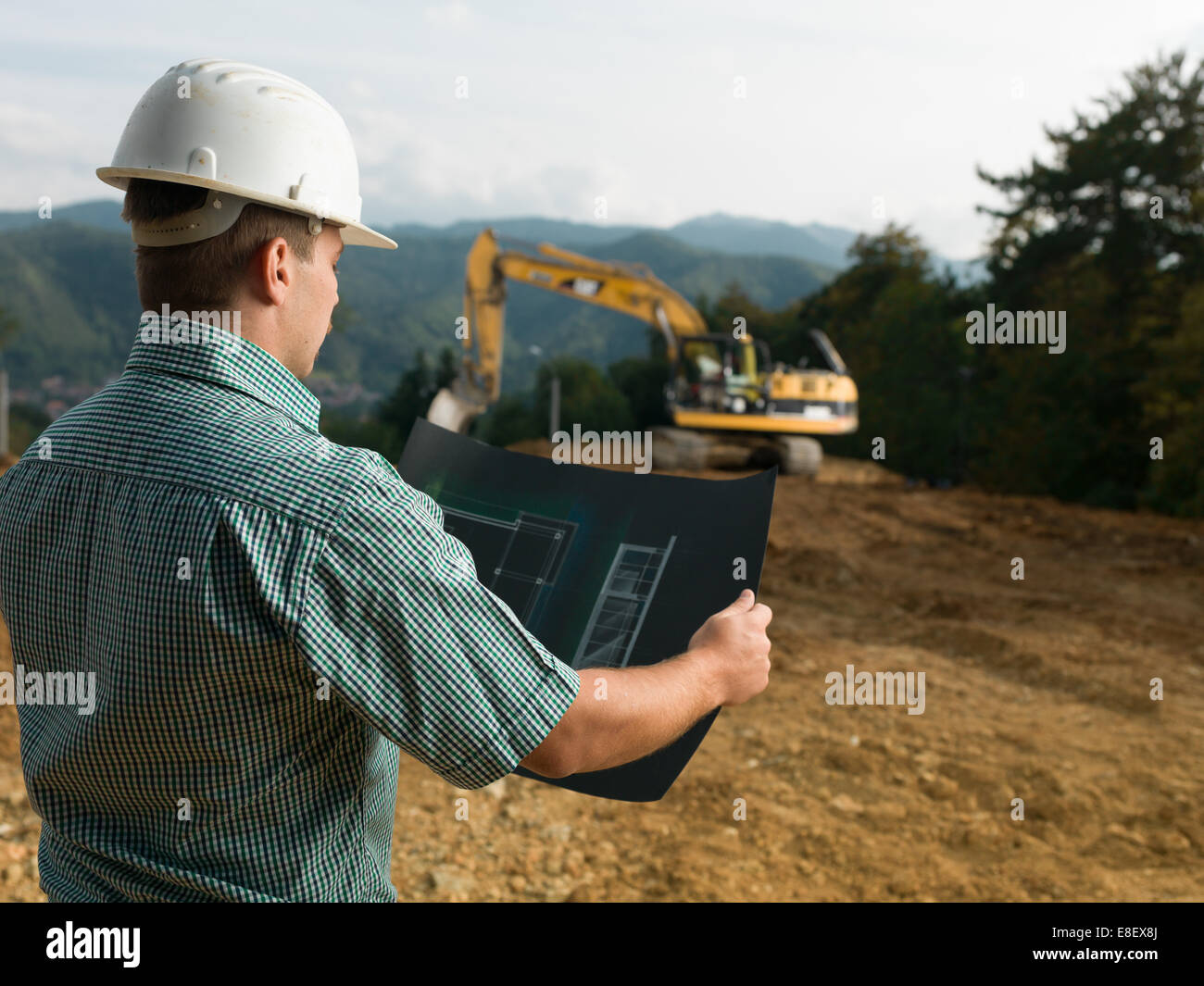 Vue arrière de l'ingénieur homme debout sur le site de construction du plan de lecture Banque D'Images Vue arrière de l'ingénieur homme debout sur le site de construction du plan de lecture Banque D'Images