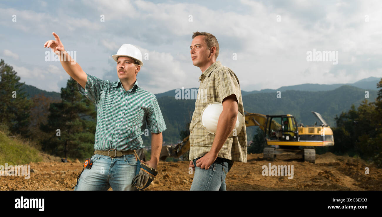 Deux ingénieurs de race blanche debout, l'un d'entre eux en cours de construction pointingat Banque D'Images Deux ingénieurs de race blanche debout, l'un d'entre eux en cours de construction pointingat Banque D'Images