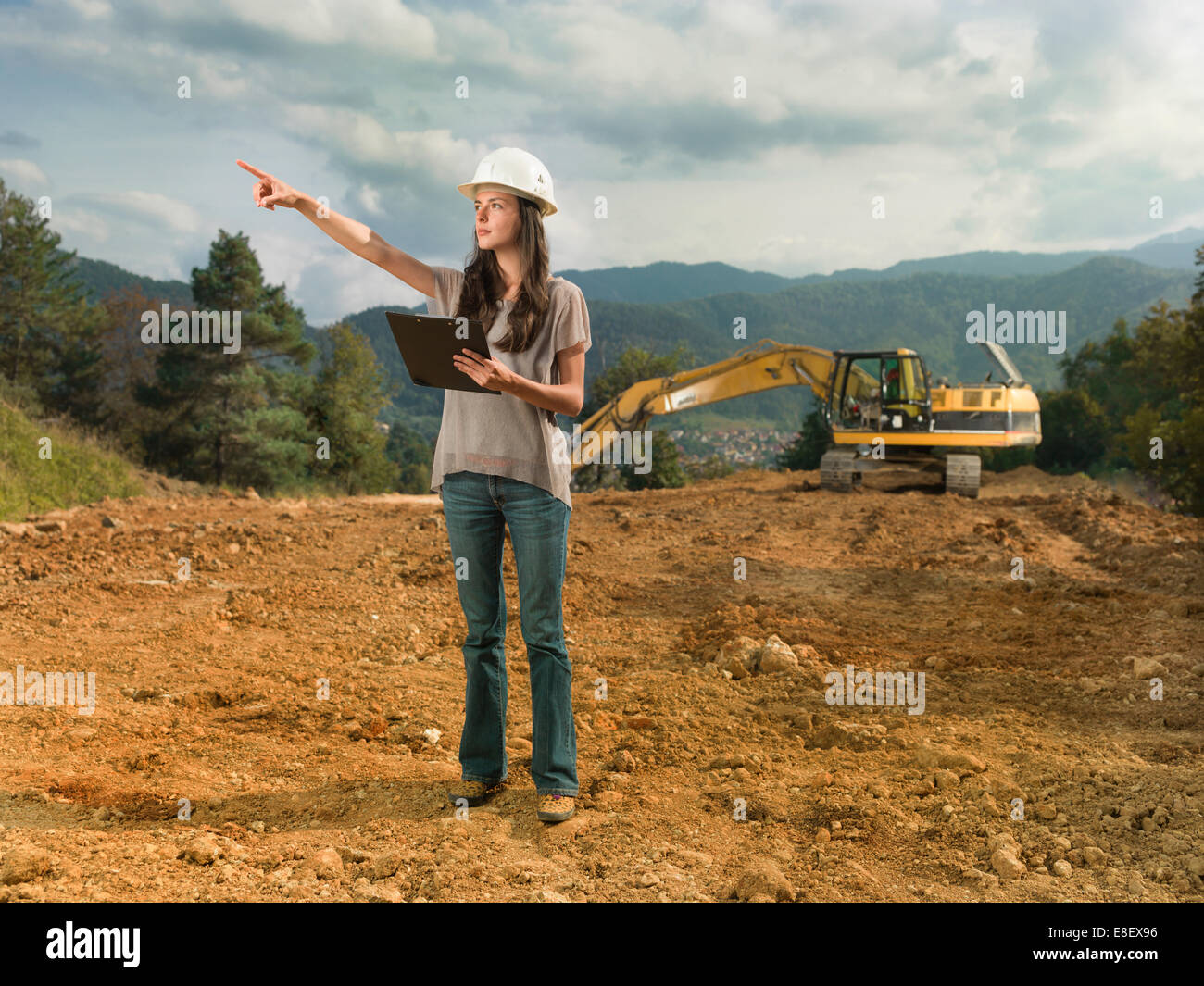 Portrait of young caucasian female architect at construction site, holding clipboard, pointant quelque chose Banque D'Images Portrait of young caucasian female architect at construction site, holding clipboard, pointant quelque chose Banque D'Images