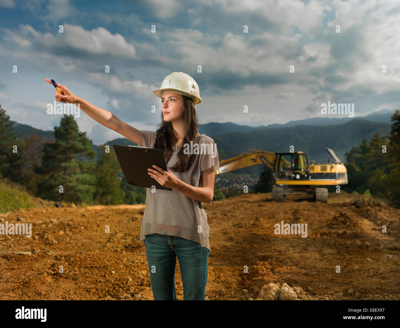 Portrait of young caucasian female architect at construction site, holding clipboard, pointant quelque chose Banque D'Images Portrait of young caucasian female architect at construction site, holding clipboard, pointant quelque chose Banque D'Images