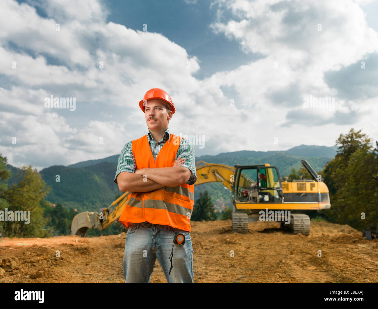 Vue avant du comité permanent de la construction ingénieur sur site en plein air avec la pelle en arrière-plan Banque D'Images Vue avant du comité permanent de la construction ingénieur sur site en plein air avec la pelle en arrière-plan Banque D'Images
