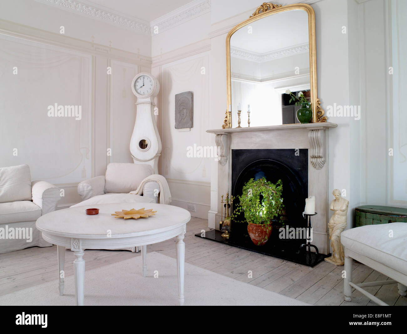 Table basse laqué blanc en face de la cheminée de marbre avec grand miroir doré dans un style suédois dans tous les salon blanc Banque D'Images